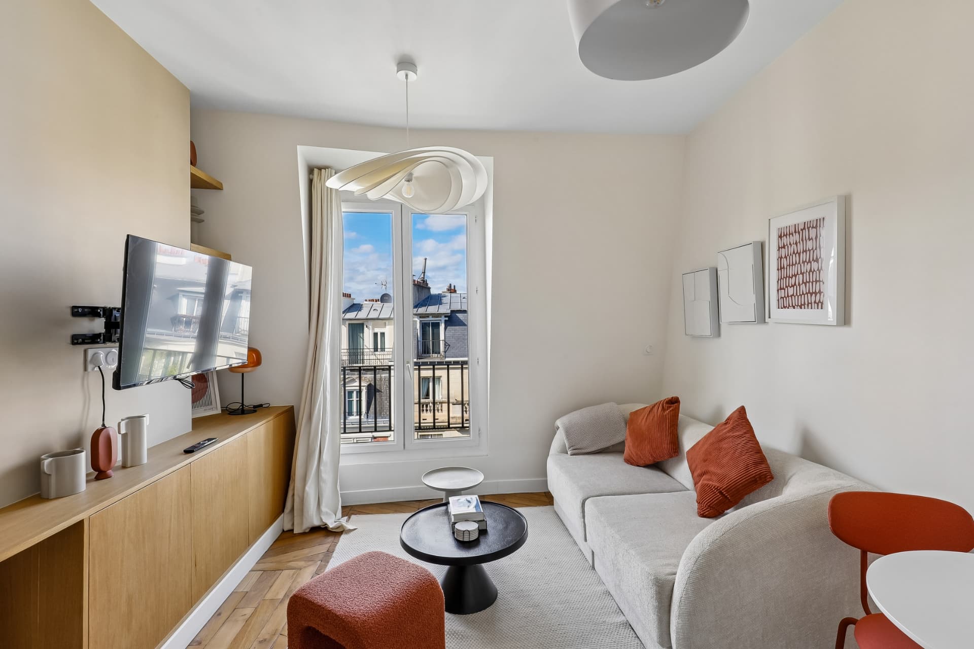 Séjour du lot 20 avec canapé gris, coussins terracotta et porte-fenêtre ouverte sur le balcon