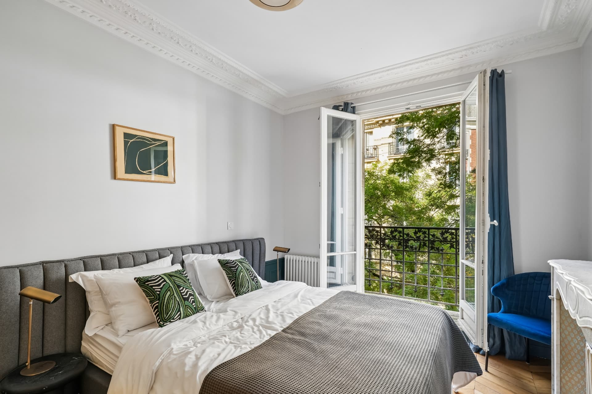 Chambre du lot 10 ouverte sur le balcon, tête de lit grise et fauteuil bleu