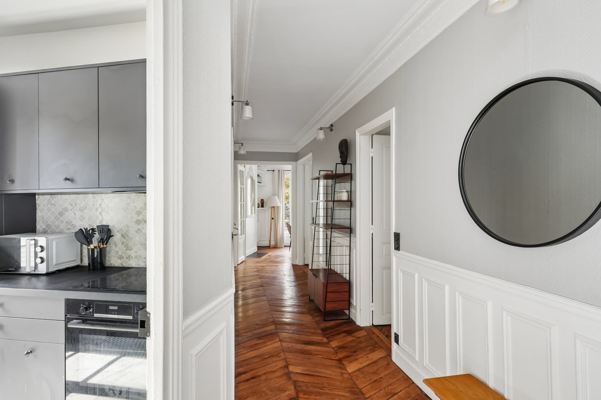 Entrée du lot 7 avec miroir rond, bibliothèque et vue sur la cuisine