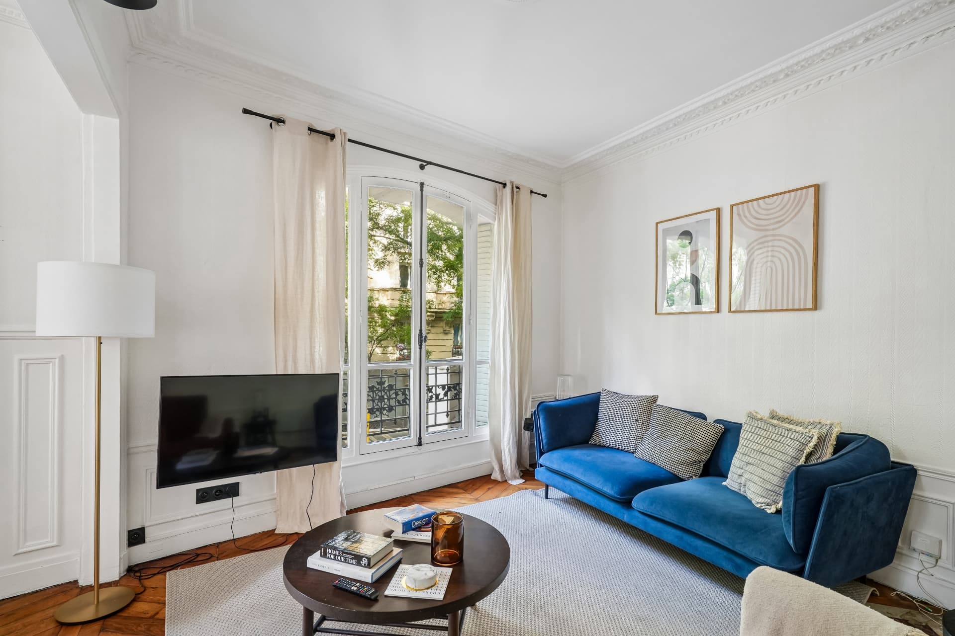 Séjour du lot 7 avec canapé bleu, télévision et porte-fenêtre sur balcon